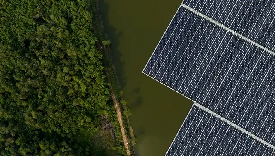Aerial view of floating solar panels on a body of water beside a dense green forest.