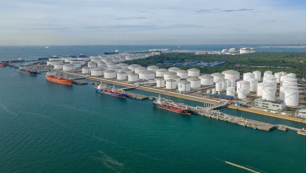 Industrial refinery complex along the waterfront with multiple chimneys emitting steam, illustrating large-scale energy production and infrastructure.