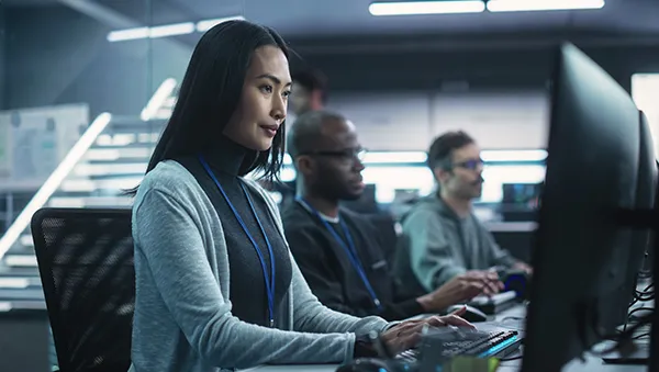 Focused professionals working at computer stations in a modern tech office environment.