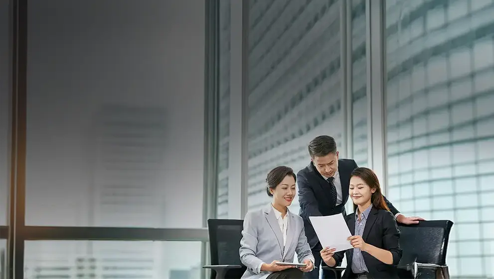 Three business professionals discussing documents in a bright, modern office, representing strategic planning and professional collaboration.
