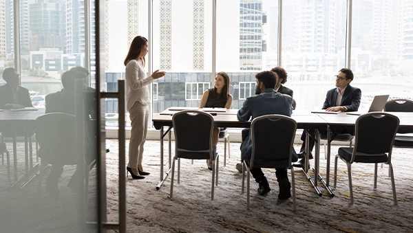 A businesswoman presents to a group of professionals in a modern conference room, illustrating policy leadership and strategic discussion.