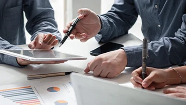 Business professionals discussing project financing strategies with digital tablet and printed charts during a meeting.