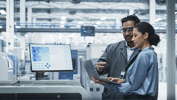 Two engineers reviewing data on a laptop in a high-tech facility, representing a skilled semiconductor workforce.