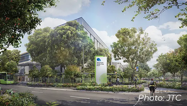 Lush, green industrial park with a cyclist and modern building, symbolizing sustainable land use for the semiconductor industry.