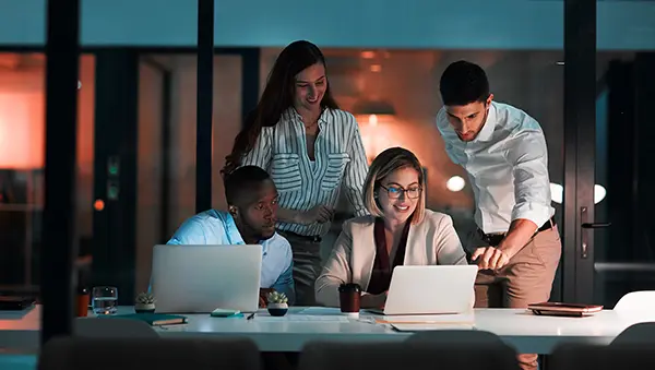 Diverse group of professionals collaborating around a laptop in a modern office, representing a global talent workforce.