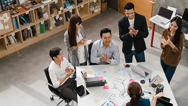 Team of young professionals in a creative office space celebrating a successful brainstorming session, showcasing specialized work schemes and collaboration.
