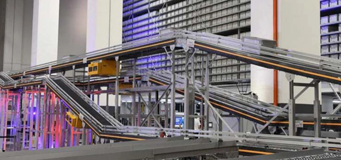 A high-tech automated warehouse featuring an intricate system of conveyor belts and robotic tracks, designed for efficient sorting and transportation of goods. The background includes towering storage racks filled with uniform bins, illuminated with blue and red accent lighting.