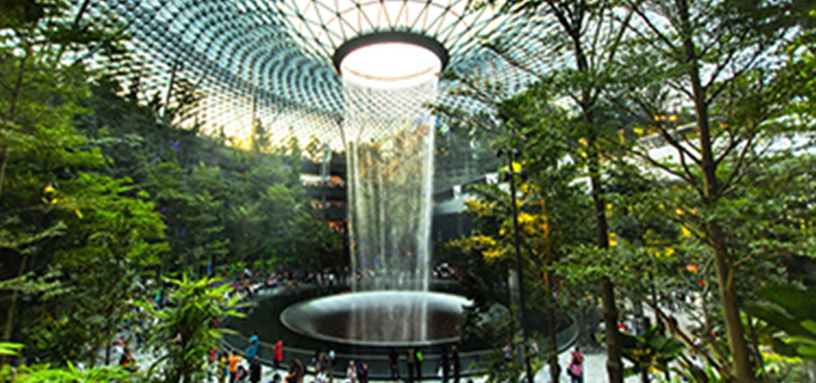 Indoor forest scene at Jewel Changi Airport featuring the Rain Vortex, the world’s tallest indoor waterfall, cascading from a glass dome surrounded by lush greenery and visitors.