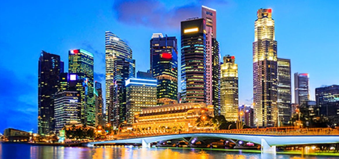 Singapore skyline at dusk with illuminated skyscrapers and a bridge over Marina Bay, symbolizing vibrant urban development and economic vitality.