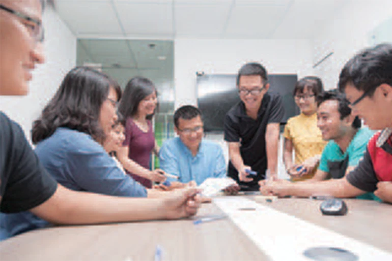 Group of colleagues gathered around a conference table, smiling and collaborating, symbolizing teamwork and a positive work environment.