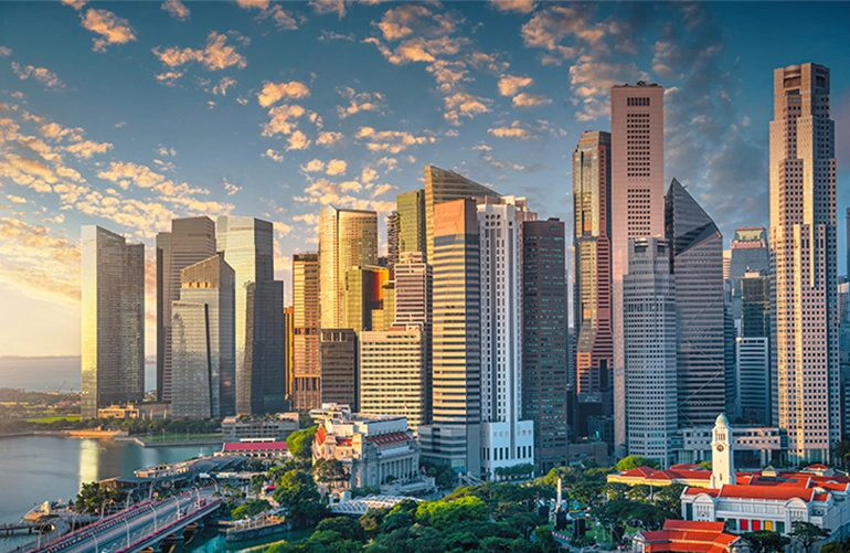 Scenic view of Singapore’s Marina Bay skyline during sunset, featuring a cluster of modern skyscrapers and historic buildings with a vibrant sky overhead.