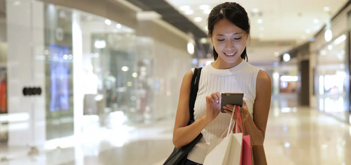 A lady checking on her phone while smiling in the mall.