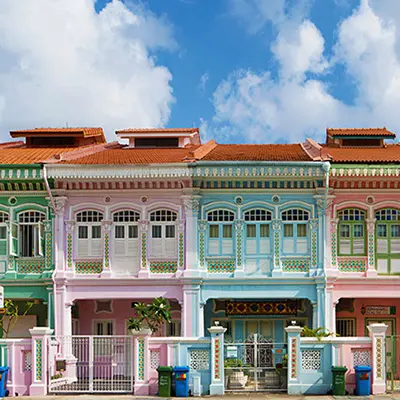 Row of colorful Peranakan shophouses with ornate facades and pastel tones, showcasing traditional architecture under a bright blue sky.