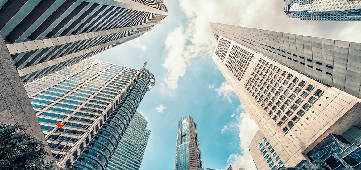 Upward view of tall modern skyscrapers framing a blue sky with scattered clouds.