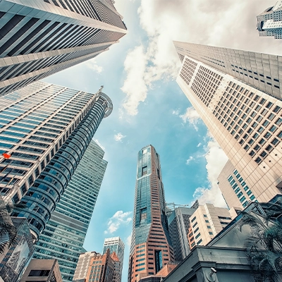 Upward view of tall modern skyscrapers framing a blue sky with scattered clouds.