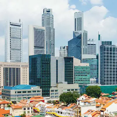 A vibrant view of Singapore’s central business district showcasing a dense cluster of modern skyscrapers contrasted with the traditional shophouses featuring red-tiled roofs in the foreground under a partly cloudy sky.