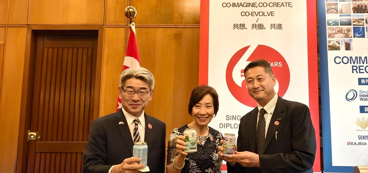 Three people holding commemorative items at a Singapore-Japan diplomatic event.