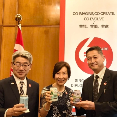 Three people holding commemorative items at a Singapore-Japan diplomatic event.