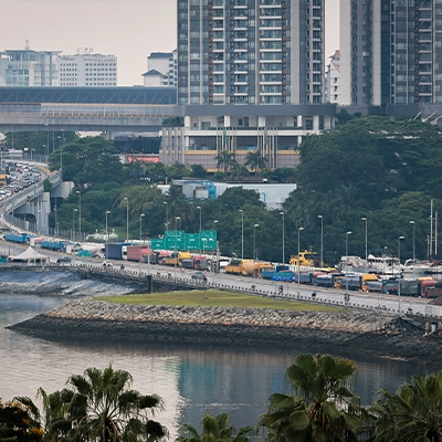 Heavy traffic congestion along the Johor–Singapore Causeway with trucks and vehicles entering Johor Bahru, against a backdrop of high-rise buildings and waterfront areas.