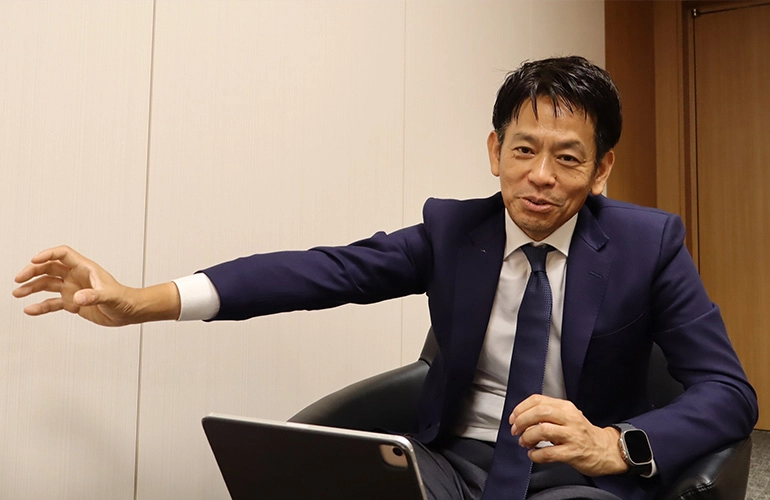 Man in a suit speaking during an interview, with a tablet in front of him.