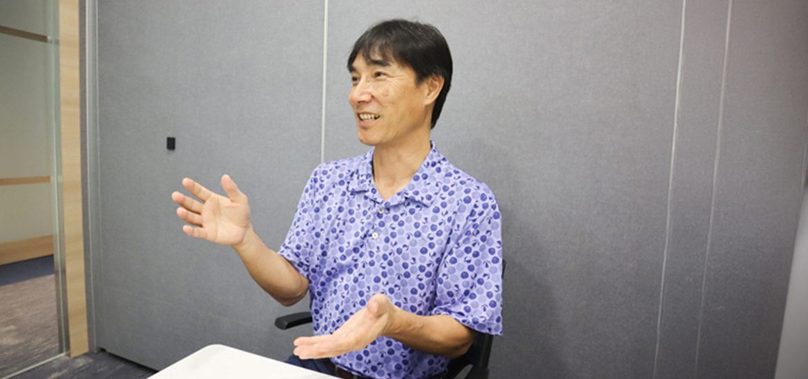 Man speaking during an interview or discussion in an office meeting room, gesturing with his hands while seated at a table.