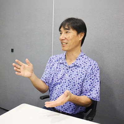 Man speaking during an interview or discussion in an office meeting room, gesturing with his hands while seated at a table.