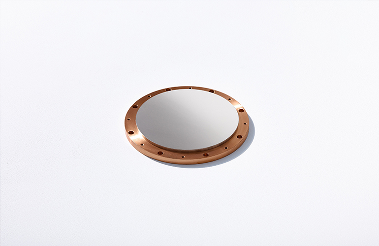 Circular metal sputtering target component with a polished reflective surface and copper-colored outer ring displayed against a white background.