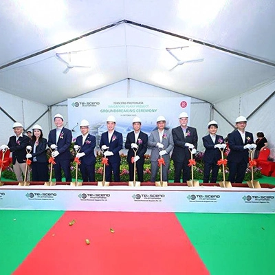 Group of executives in formal attire and safety helmets holding ceremonial shovels at the Tekscento Photomask Singapore project groundbreaking ceremony.