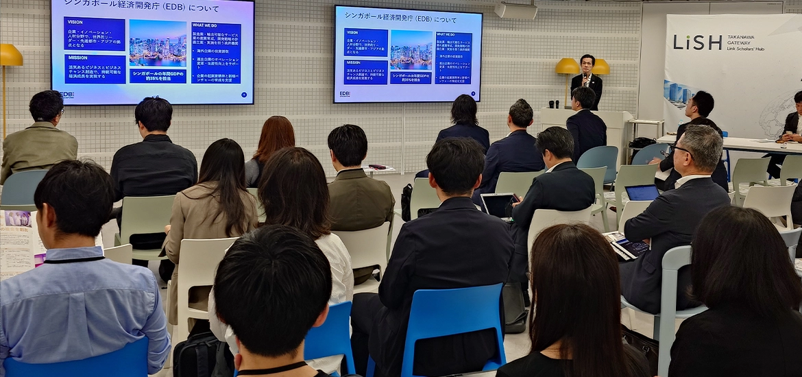 Audience attending a business presentation on Singapore’s Economic Development Board (EDB), with a speaker presenting slides on large screens in a conference room.