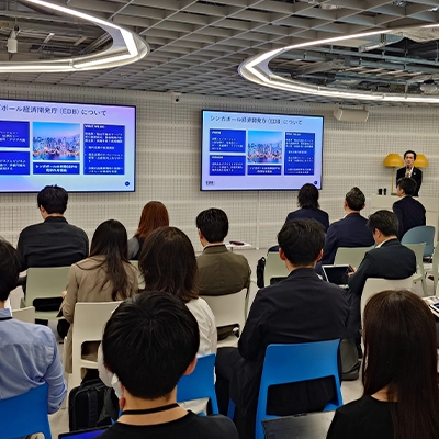 Audience attending a business presentation on Singapore’s Economic Development Board (EDB), with a speaker presenting slides on large screens in a conference room.