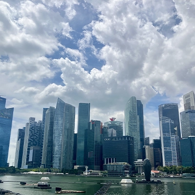 Singapore’s central business district skyline with modern skyscrapers along Marina Bay, reflected in the water under a cloudy sky.