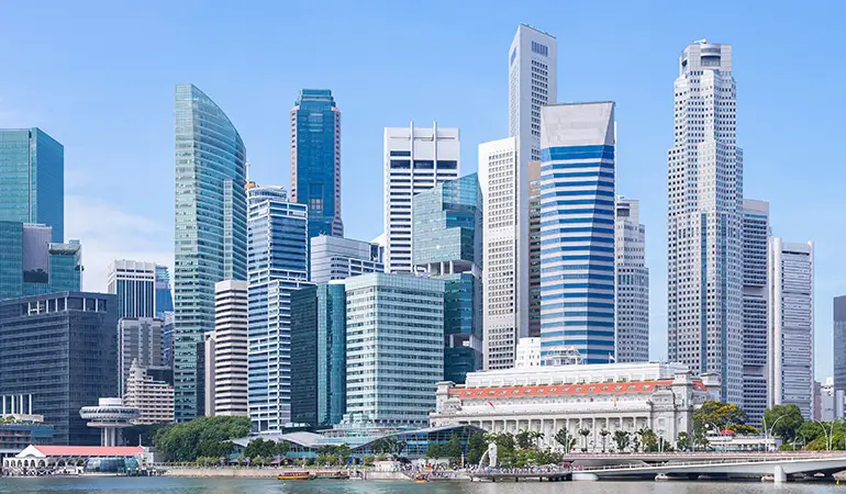 Skyline view of Singapore’s Central Business District featuring modern high-rise office buildings and iconic architecture under a clear blue sky, with the Fullerton Hotel and waterfront promenade in the foreground.