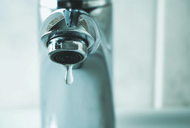Close-up of a water droplet falling from a chrome faucet.