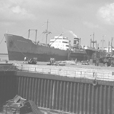 Black-and-white historical view of Singapore’s skyline with numerous boats anchored in the harbour.