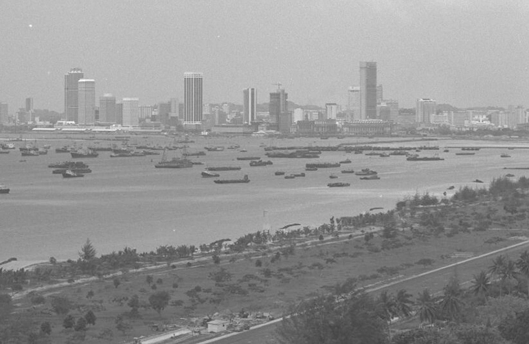 Black-and-white historical view of Singapore’s skyline with numerous boats anchored in the harbour.