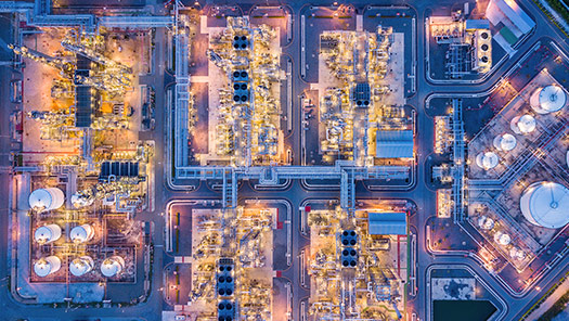 Aerial view of a large industrial plant at night, showcasing illuminated processing units, pipelines and storage tanks arranged in a grid layout.
