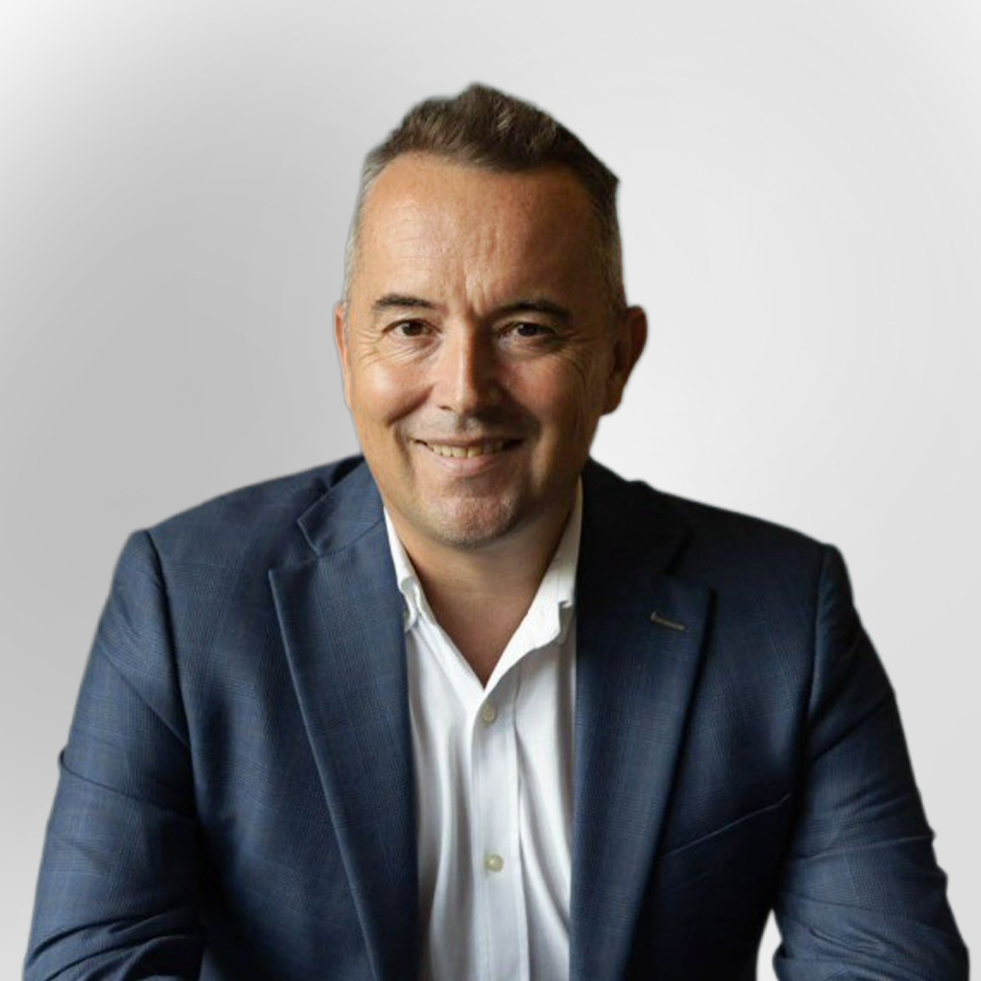 Portrait of a man in a blue blazer and white shirt smiling against a plain background.