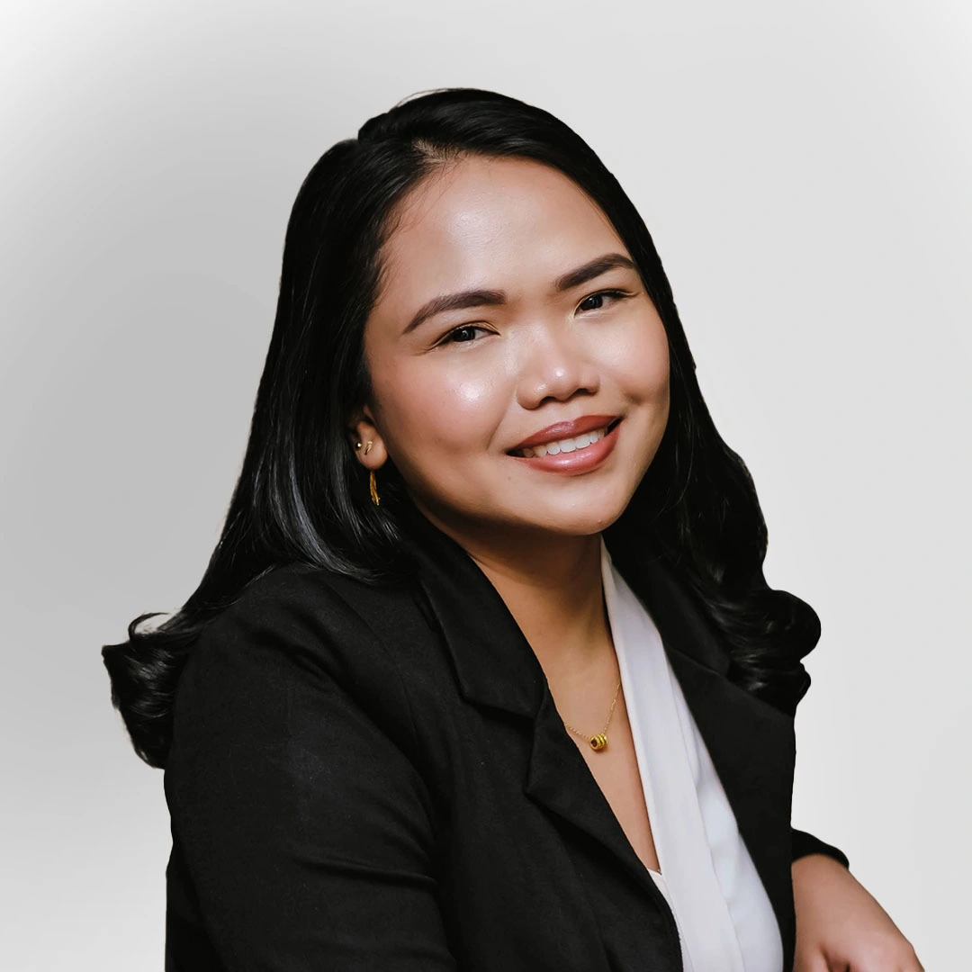 A smiling woman in business attire, wearing a black blazer and light top, posed against a plain background.