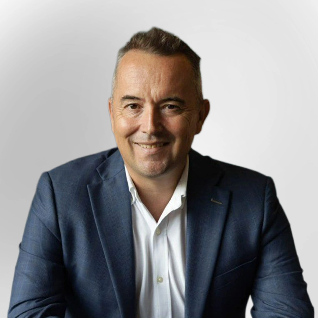 Portrait of a man in a blue blazer and white shirt smiling against a plain background.