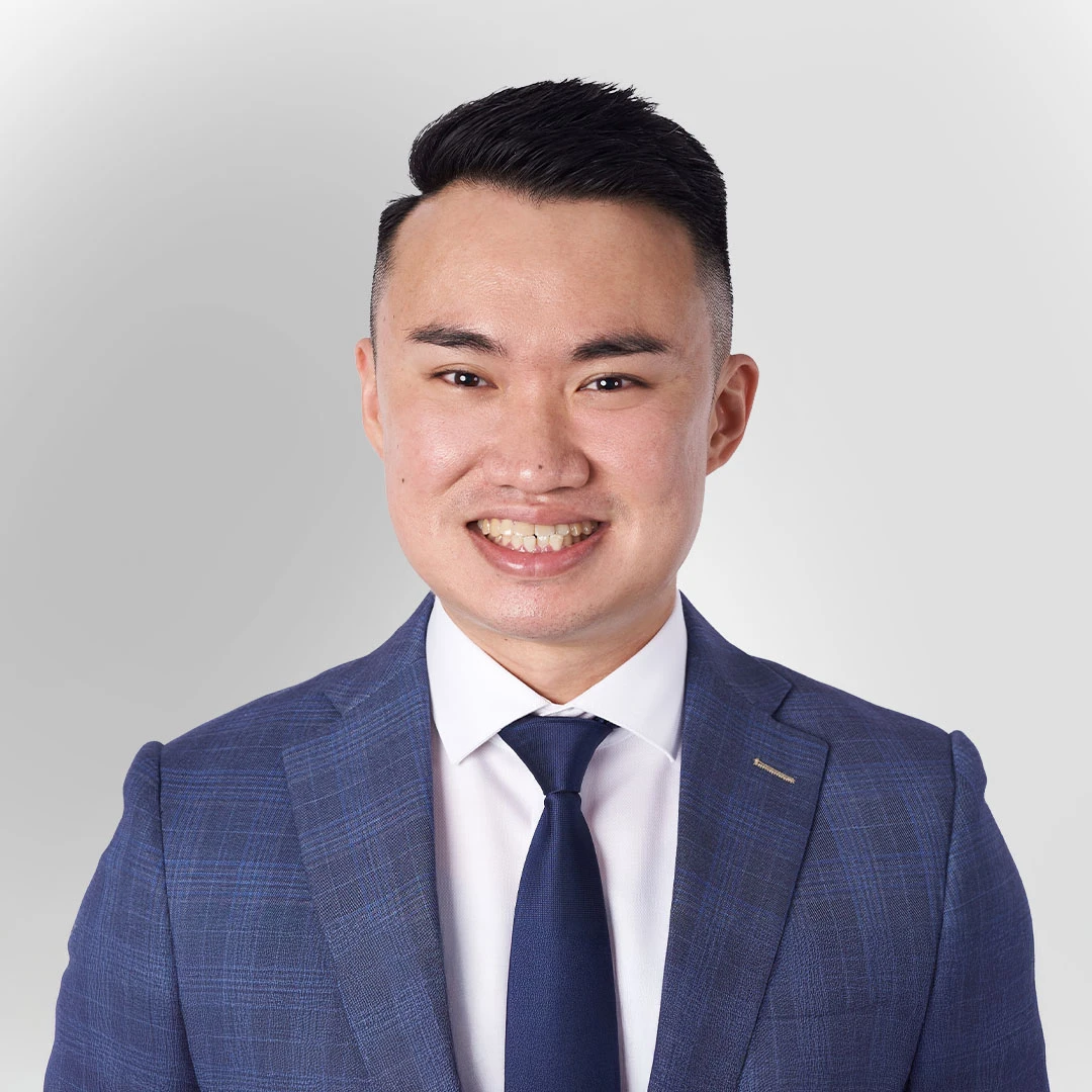 Portrait of a man in a blue suit and tie smiling against a plain background.