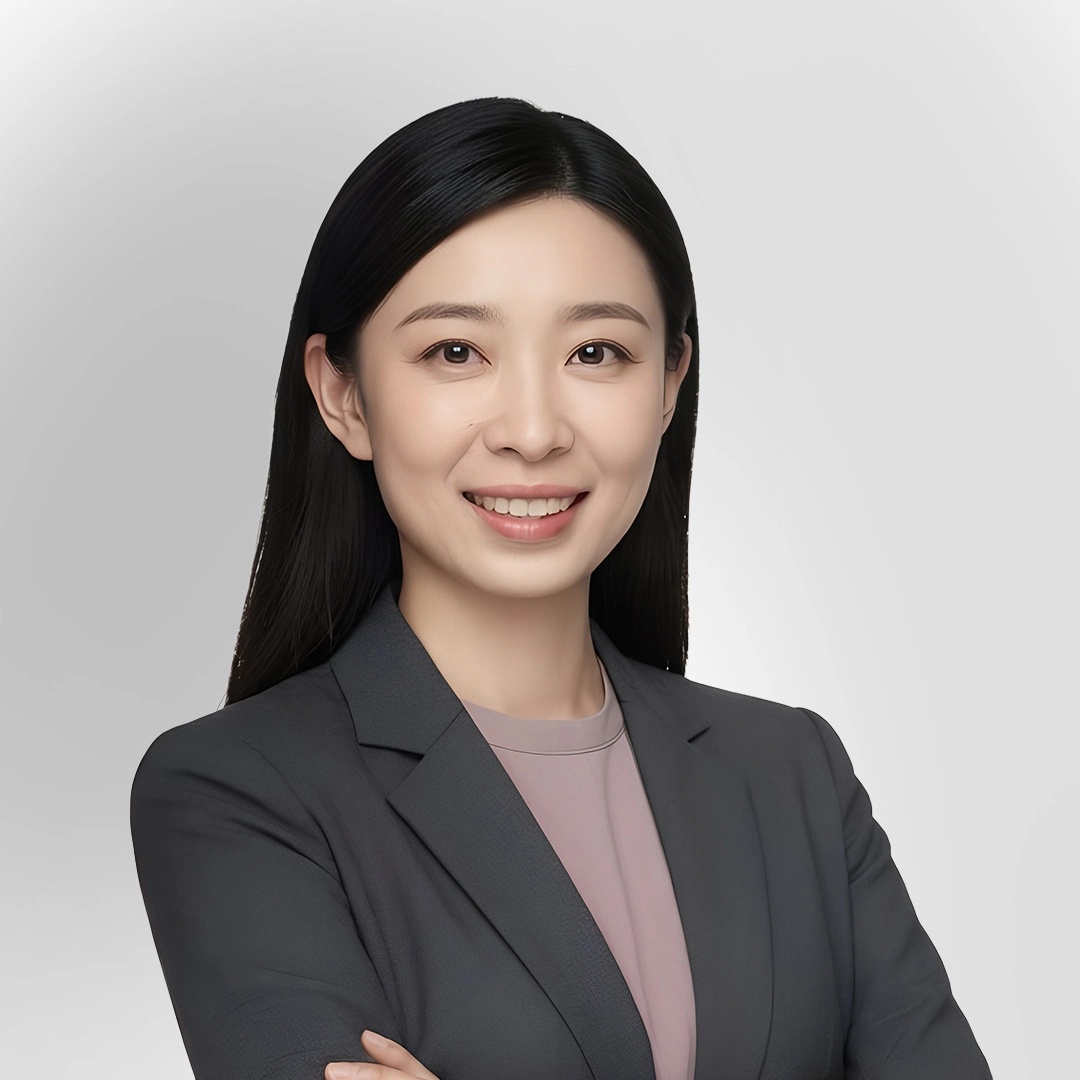Portrait of a woman in a grey blazer smiling with arms crossed against a plain background.