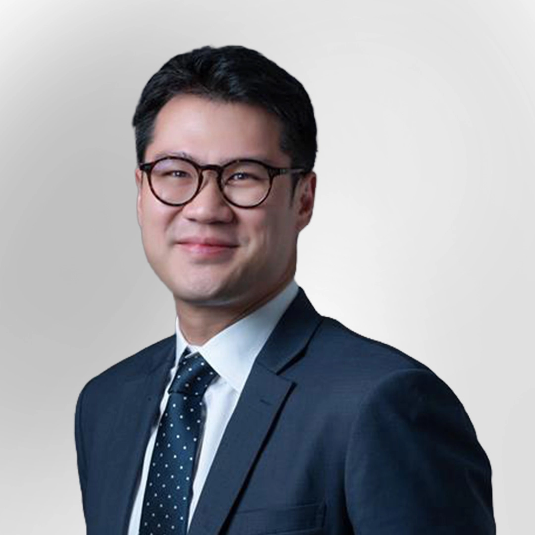 Portrait of a man wearing glasses, a suit, and a tie, smiling against a plain background.