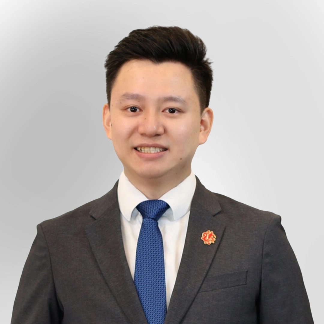 Portrait of a man in a suit and blue tie smiling against a plain background.